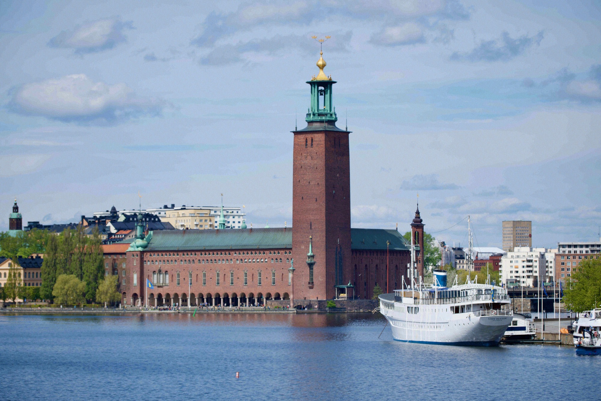 Das Stockholmer Rathaus (Stadshuset) mit seinem markanten Backsteinturm und goldener Krone vom Mälaren aus fotografiert.