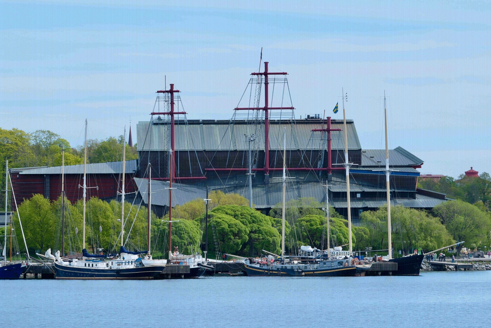 Das Vasamuseet auf Djurgården vom Wasser aus gesehen, mit den charakteristischen roten Masten des Kriegsschiffs Vasa, die über das Dach ragen.